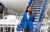 Businesswoman at the airport carries a suitcase, prepares to board the plane and depart. Asian female tourist at airport using smartphone to contact someone.