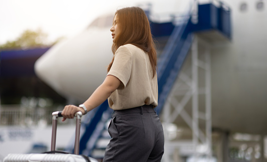 Asian businesswoman holding a bag is walking up the airplane stairs. Happy young female traveler from an unforgettable trip in Asia.