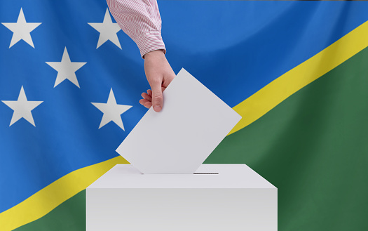 Elections, Solomon Islands. Election concept. A hand throws a ballot into the ballot box. Flag of Solomon Islands on background.