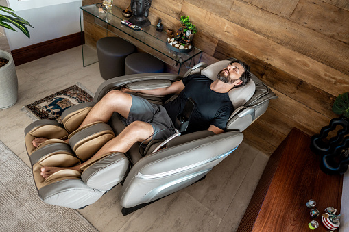 Mid adult man sleeping on a massage chair at home