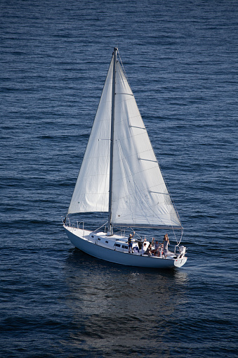 A light blue sailboat is sailing peacefully in Frenchman Bay around the porcupine islands in Bar Harbor Maine.