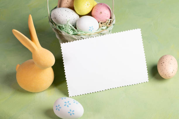 istock White blank note on pastel yellow green backdrop surrounded by color Easter eggs and yellow bunny. 2148157555