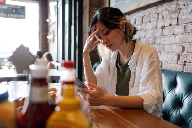 istock Pensive woman sitting by a restaurant and texting annoyed on mobile 2148158235