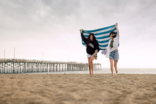 Two friends running away from the beach while is raining.