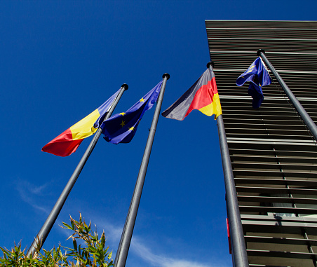 Bucharest, Romania, Europe - March 29, 2024 - Romanian Flag, German Flag and European Union Flags Blue Sky Spring Cityscape, Leonardo Hotel Bucharest City Center in the Background, Victory Avenue 1st District (Bucharest Stock Exchange Victory Square Financial District, Romanian Athenaeum Concert Hall, National Museum of Art of Romania and the Palace of the Parliament in the Neighborhood), Historic City Center, Southeastern Romania, European Union, Southeastern Europe