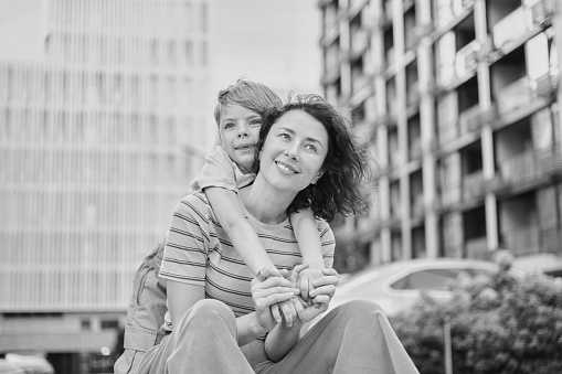 young mother and son smiling looking at the camera in modern residential complex. Having fun together, happy parenting, new home concept. Bright summer day in the urban background. High quality photo