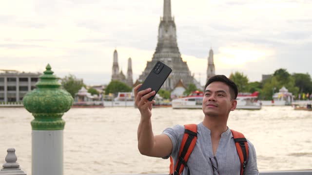 man taking selfie when  Exploring in beautiful temple at Wat Arun which alongside Chao Phraya river on holiday in Bangkok, Thailand. For Summer or Holiday concept background.