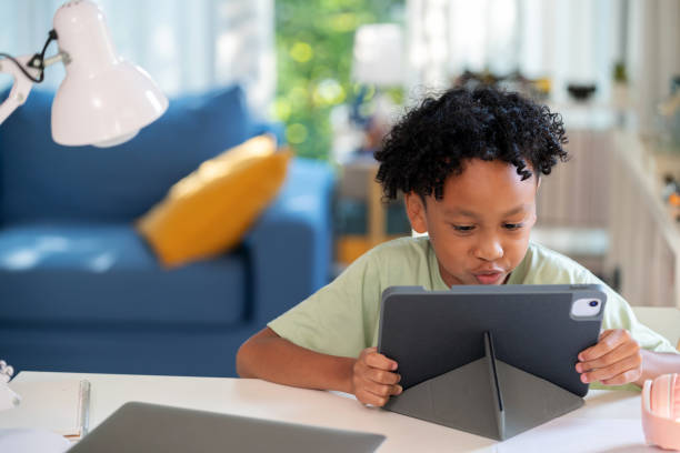 istock Studying Online with Digital Tablet. Cheerful boy wearing headphones sits happily with smile in the living room, studying online e-learning using a digital tablet. Engaged and focused, he enjoys his e-learning experience. 2148162964