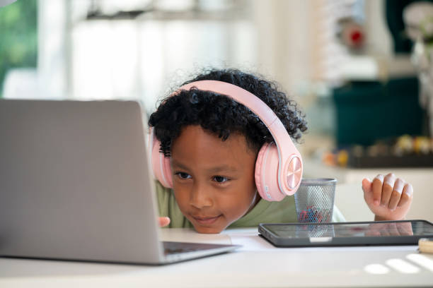 istock Studying E-Learning on Computer at Home. Cheerful black boy is sitting in his living room, wearing headphones and engrossed in e-learning on computer. With a bright smile, he demonstrates the joy and enthusiasm of online learning. 2148162977