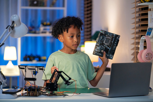 Confident black boy is livestreaming from his living room, passionately explaining the workings of a mainboard. This image reflects the modern era where children have quick and easy access to technology, fostering curiosity, learning, and innovation. Perfect for showcasing the enthusiasm of young learners and the power of online platforms.