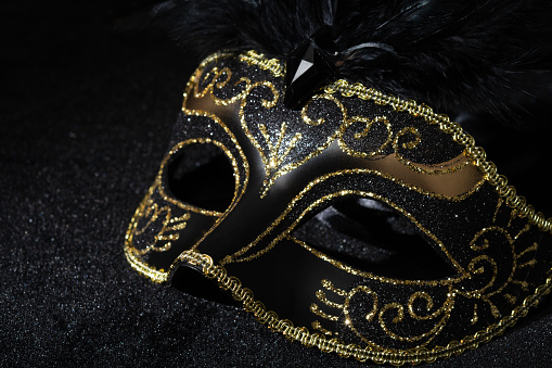 Close-up view of Masquerade gold mask with feathers on black background.