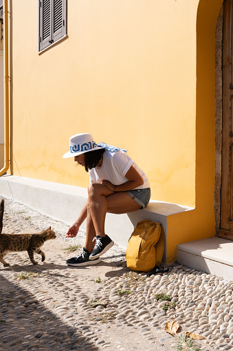 Woman sitting resting in the central and beautiful street of the ancient city of Rhodes while petting a small stray kitten
