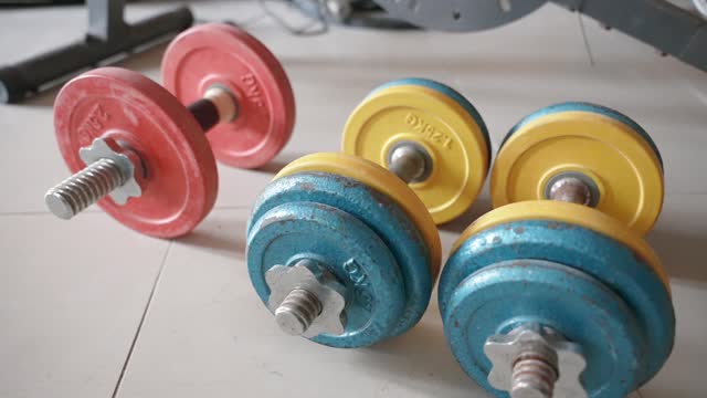Close up of the colored heavy adjustable dumbbell set lying on the floor in the living room. Home gym equipment