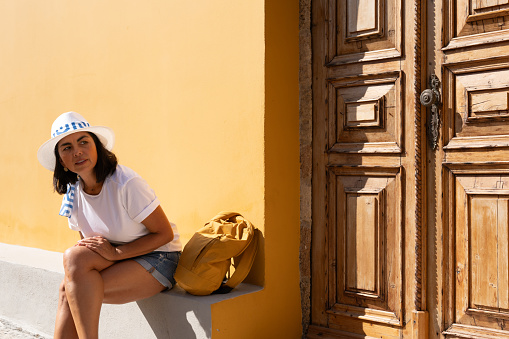 Beautiful woman with greek hat sitting while enjoying the beauty of the old and medieval town of Rhodes on her trip through Greece in summer