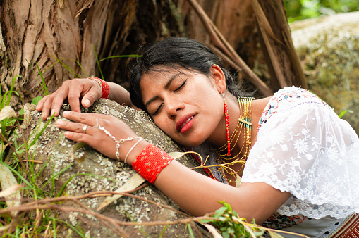 indigenous woman from Ecuador resting on a rock between trees and vegetation connecting with mother nature. national hispanic heritage month
