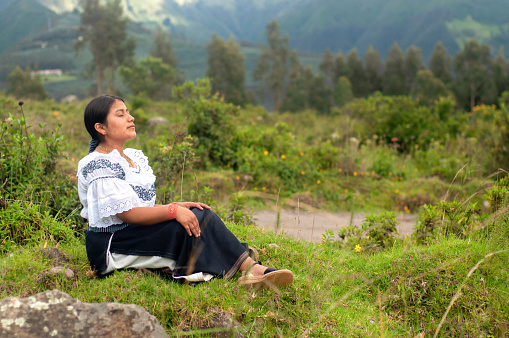 Woman in traditional dress enjoying a peaceful moment in a mountain meadow at dusk