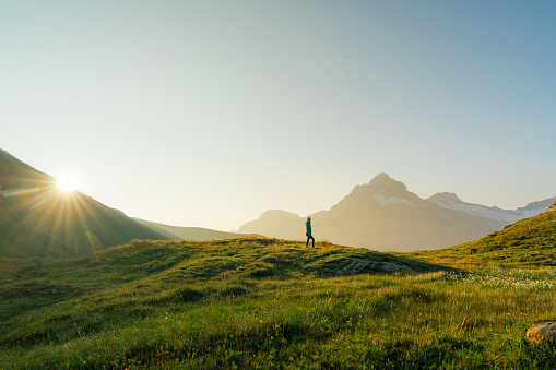 Woman hiking through the meadow  on the background of snowcapped  Swiss Alps in morning