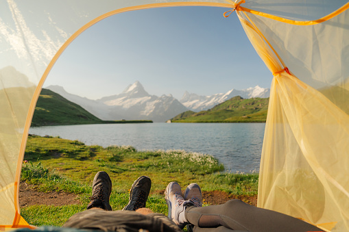 POV of man and woman laying in the tent and looking at lake in Swiss Alps in summer
