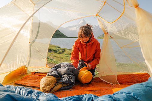 Woman packing sleeping bag after spending the night in the tent in Swiss Alps in summer