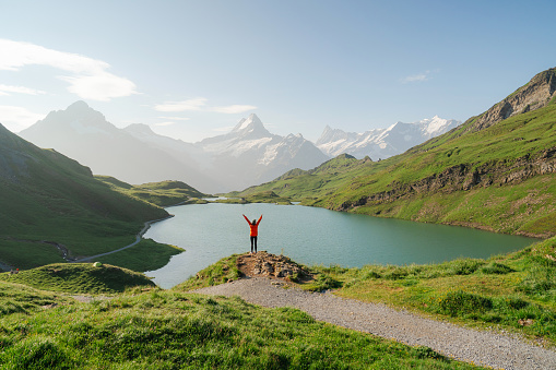 Woman standing with arms raised in awe near Bachalpsee lake in Swiss Alps in summer