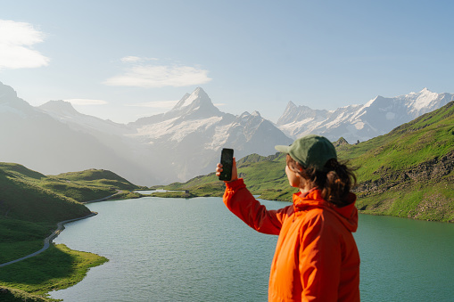 Cheerful woman photographing with smartphone near Bachalpsee lake in Swiss  alps in summer