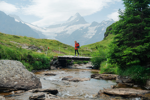 Woman with backpack hiking through the footbridge in Swiss Alps on the background of snowcapped mountain