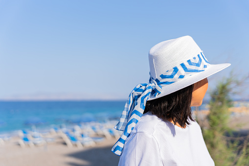 Beautiful unrecognizable woman with a Greek hat enjoying a visit to the Greek island of Rhodes next to a beach on a bright summer day