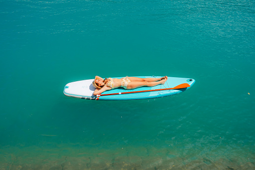 Serene scene of woman  sunbathing while SUP boarding on lake in Alps in summer