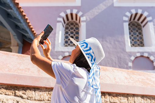 Beautiful woman with greek hat enjoying while taking a photo of the historic area of Rhodes town on her tour trip around the greek island in summer