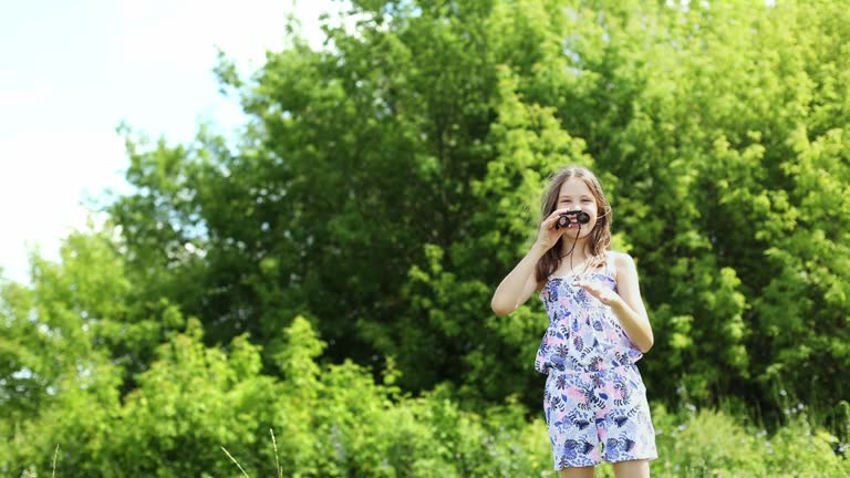 Happy teenage girl looking through binoculars and laughing merrily in summer outdoors.