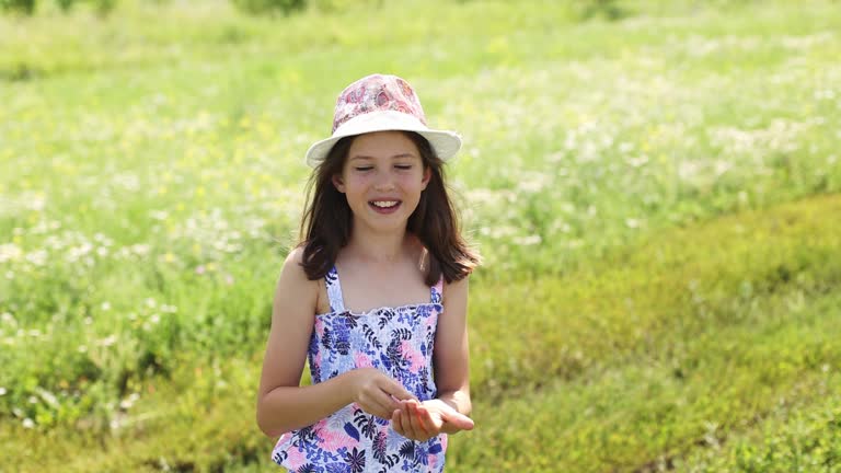 Teenage girl in a hat in summer holding a little frog in her hands.