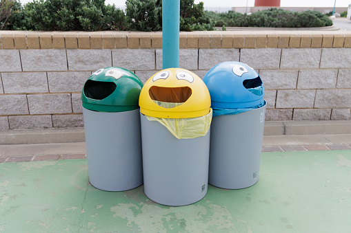 Three trash cans with faces on them. One is green, one is yellow, and one is blue