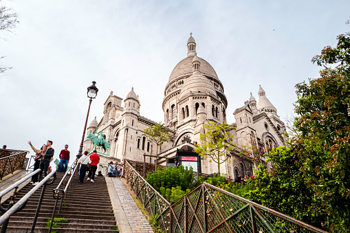 Paris, France - April 6th, 2024: The Basilica Sacre-Coeur with stairs and tourists at Paris. France