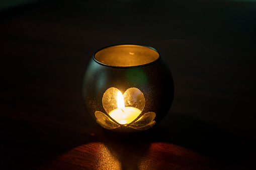 A handmade candle holder. A candle holder made of a glass jar, in the shape of a heart, stands on a table in a dark room. Valentine's Day, decoration, romantic atmosphere.