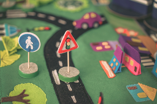 Miniature road signs and toy car on colorful play mat with felt buildings. Scene captures essence of bustling toy town.