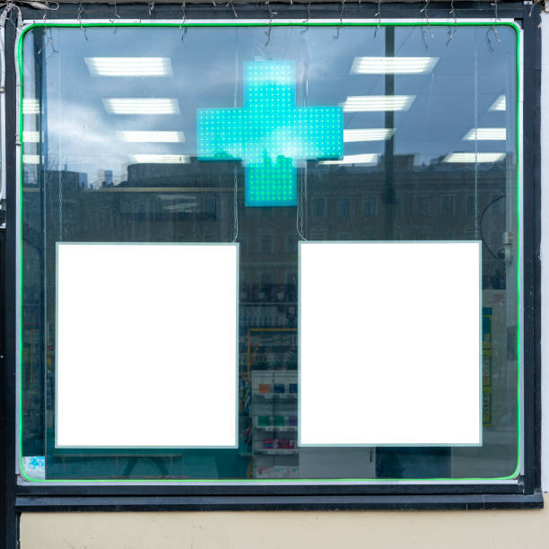 istock Pharmacy storefront with glowing green cross and two blank advertisement spaces. Reflection of urban environment on pharmacy window reveals city life outside 2148174118