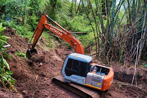 Lom Sak, Thailand, 05/12/2023. Excavator deepening a dry riverbed through a bamboo forest in the province of Phetchabun, Thailand.