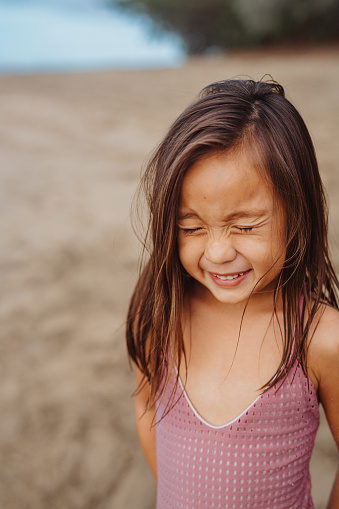 An adorable preschool age girl of Pacific Islander descent makes a silly face at the camera while standing in the sand at the beach in Hawaii.