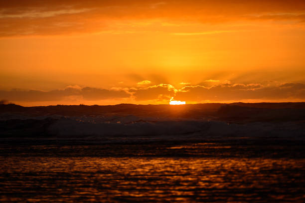 A beautiful view of an orange sun setting on the horizon of the ocean in a tropical setting.