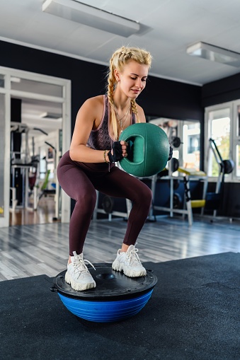 Young woman squats workout with the sports ball on balance ball in the gym