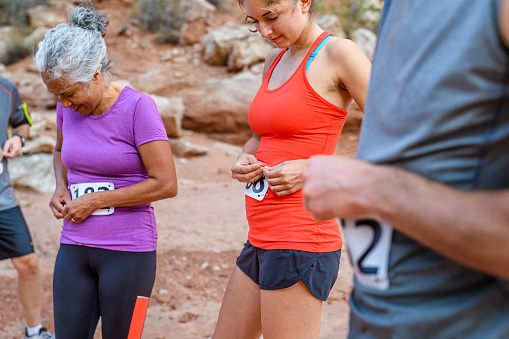 A biracial group of athletes stand outside together as they attach numbered tags to their shirts before a race on a beautiful day in Utah.