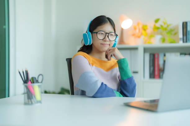 istock A young woman or student using a Laptop computer in the library while wearing glasses and headphones. She is smiling and looking happy. 2148179982