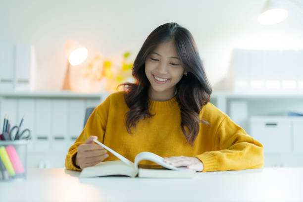 istock A young woman or student reading a book in the library while wearing glasses, She is smiling and looking happy. 2148179986