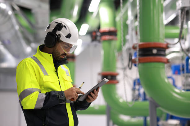 Male Industrial Engineers working with Project Blueprints drawing at front heavy industrial machinery, HVAC system engineer