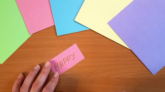Happy. Woman's hand writes words with a marker on pink paper.