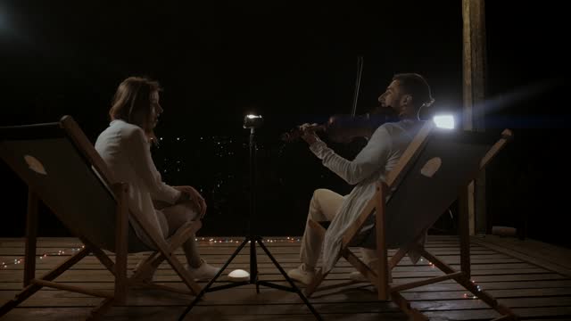 A man plays the violin and a girl sings at a concert on the street at night. A duo of musicians plays under the night sky. Musicians play on the stage of the restaurant.
