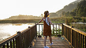 Young beautiful woman greets the sun on the pier on Lake Efteni, The young woman's arms are stretched out by the lake, She opens her arms towards the sunrise, Beautiful young woman relaxing in nature