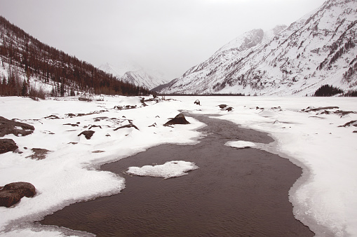A picturesque natural landscape of a frozen river surrounded by snowy mountains. Northern snowcovered river in the mountains.