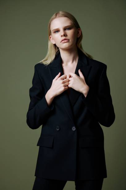 istock The model holds the jacket by the collar while posing on a green background in the studio. Concept photo for clothing brands. Cool offer for fashionable suits 2148185435