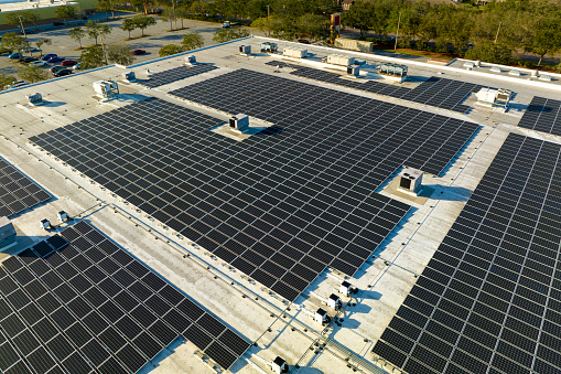 Aerial view of blue photovoltaic solar panels mounted on industrial building roof for producing green ecological electricity. Production of sustainable energy concept.